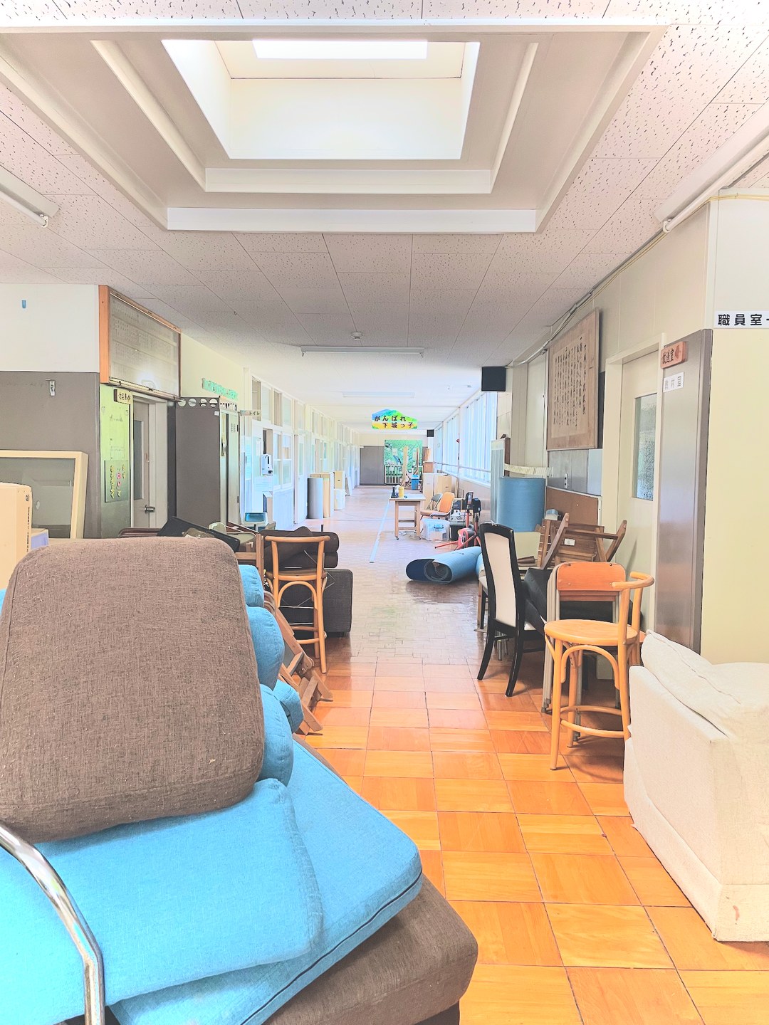 避難所となっている施設の廊下。ソファや椅子、家具が運び込まれ、奥で人が作業している