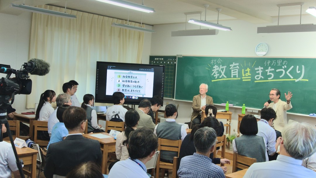 伊万里高校の教室で開かれた講座の様子。黒板に「社会教育 教育は まちづくり 伊万里の」の文字があり、左のモニターには「1 社会教育とは、2 社会教育の魅力、3 学びあい・つなぎあい、4 教育は、まちづくり」と映っている。話し手と聞き手が並び、手前に参加者が座っている